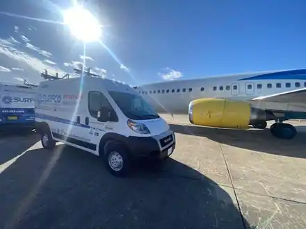 Two Surfco vans parked beside a passenger jet on an airport apron