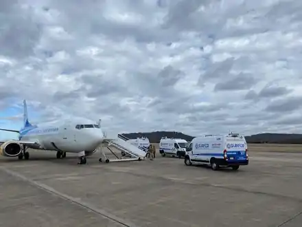 Surfco vans parked beside a passenger jet while a Tyvek-suited crew works the boarding stairs.