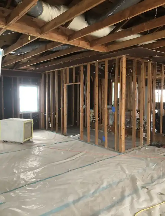 Open wall framing with plastic sheeting laid on the floor and exposed joists overhead
