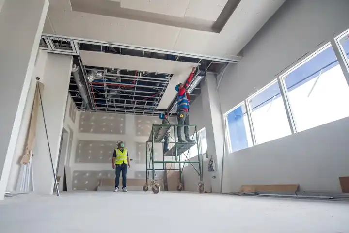 Commercial build-out with tall windows, a ceiling grid going in and a lift standing on the floor