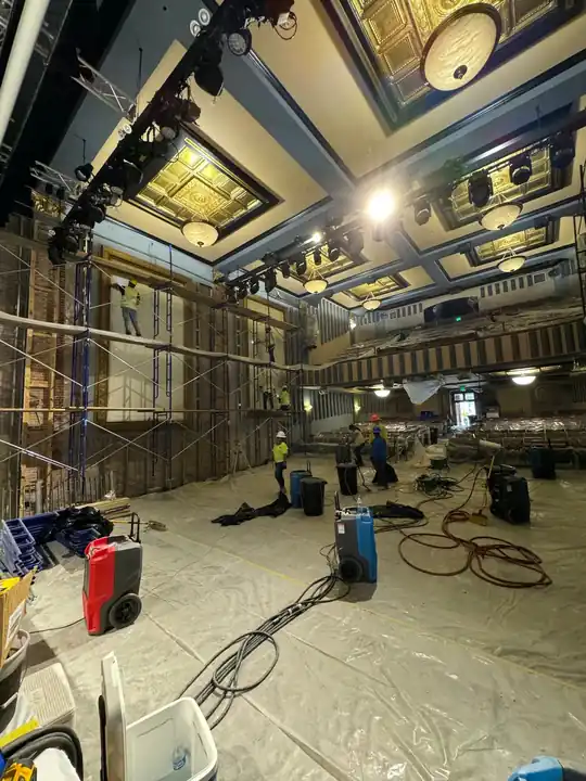 Red dehumidifier and blue air movers on plastic sheeting under a coffered theater ceiling during a Surfco restoration