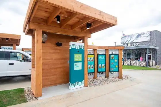 Covered wooden drive-up menu canopy with menu boards in front of a Hawaiian Bros restaurant