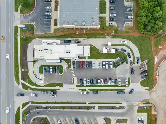 Aerial view of a Hawaiian Bros restaurant, its parking lot and the drive-through loop beside a main road