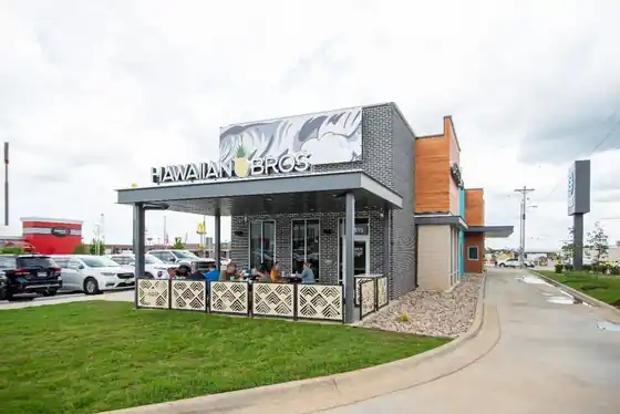 Hawaiian Bros restaurant with a covered patio, outdoor seating and a parking lot