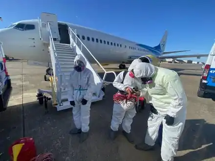 Crew members in white Tyvek suits and respirators standing at the foot of an aircraft's boarding stairs