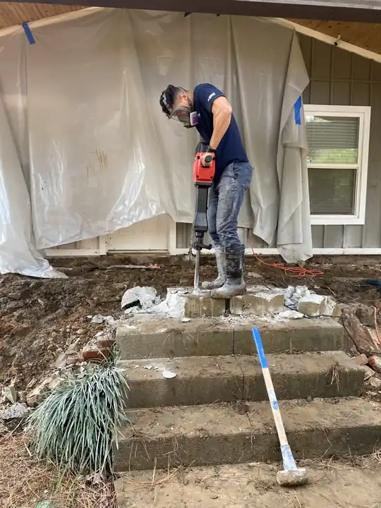 Surfco worker jackhammering concrete steps with plastic sheeting hung over the wall behind