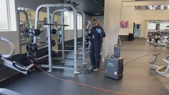 Surfco technician with a sprayer cart beside a weight machine in a gym
