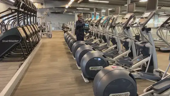 Surfco crew member disinfecting a row of elliptical machines in a large gym