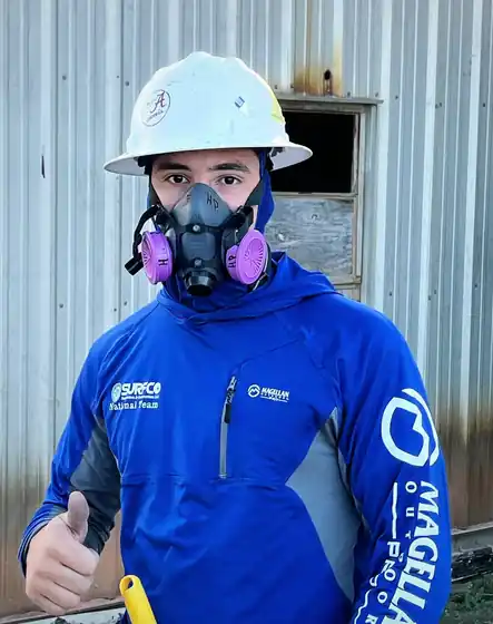 Surfco crew member in a white hard hat, half-face respirator and blue Surfco hoodie giving a thumbs up