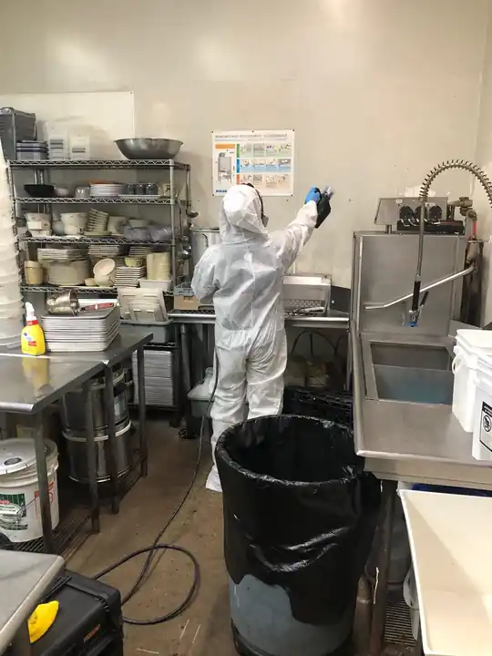 Surfco technician in a white Tyvek suit misting a commercial kitchen during a sanitizing job
