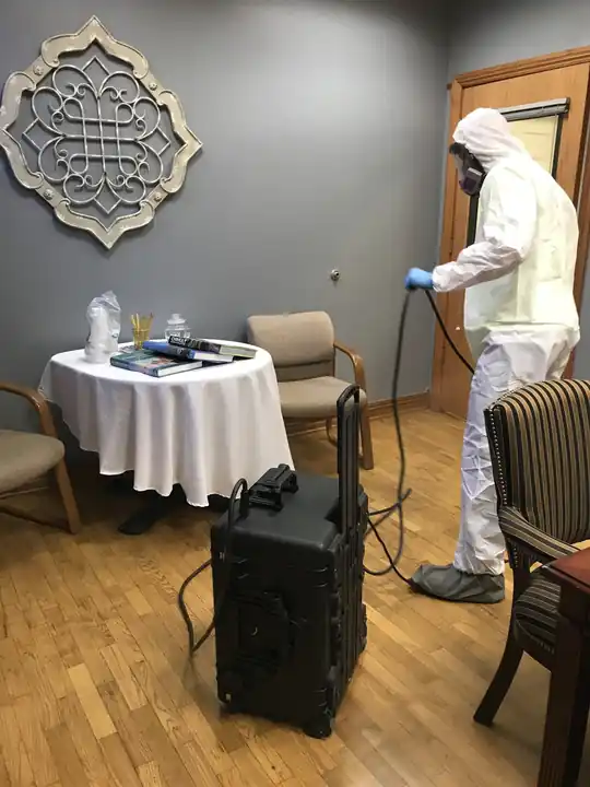 Surfco technician in a white Tyvek suit misting a conference room with a SteraMist unit