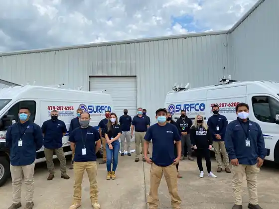 Surfco crew members in face masks and matching uniforms standing in front of two Surfco vans